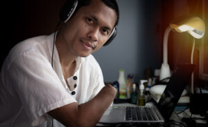 Jeune homme souriant, avec une main manquante, utilisant un ordinateur portable avec des écouteurs